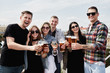 © mirage_studio - Young happy friends drinking beer before festival at outdoors pub on roof, toasting and laughing, copy space. Friendship and celebration concept