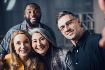 Wall Mural - selective focus of smiling multicultural colleagues looking at camera and taking selfie