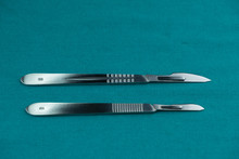 Surgical Instrument, Stainless Steel Scalpel Handle Number 3 With Blade Number 10 And Scalpel Handle Number 4 With Blade Number 24 On Surgical Green Drape Fabric.