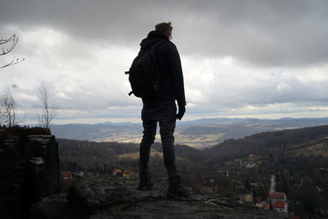 Rear view silhouette of a hiking man standing on sandstone plateau against dramatic cloudy sky in Tisa, Czechia  