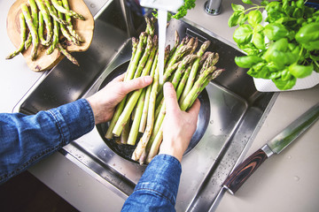 cropped shot of male hands in soil washing fresh asparagus in kitchen sink.