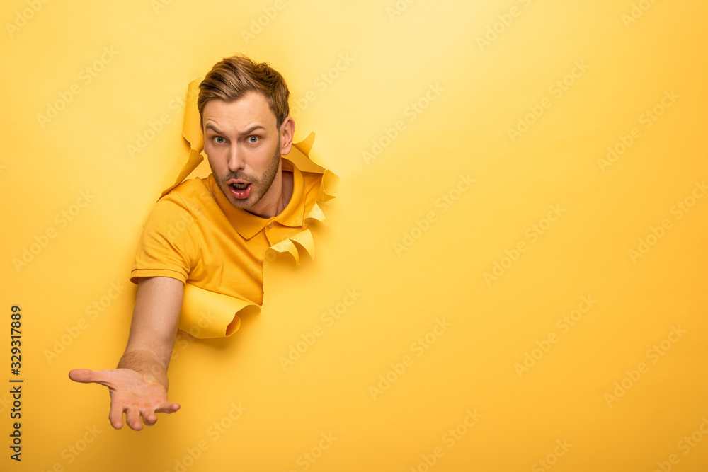 confused handsome man in yellow outfit in yellow paper hole - obrazy, fototapety, plakaty 
