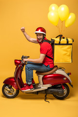 Wall Mural - side view of happy delivery man with balloons on backpack on scooter showing fist on yellow background