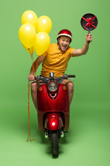 Wall Mural - happy delivery man in yellow uniform on scooter with frying pan and balloons on green