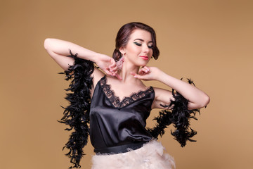 Brunette beautiful woman in black boa from ostrich feathers is dancing on beige background