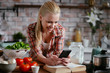 © JustLife - Beautiful woman in kitchen. Young woman writing message on phone.