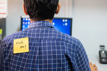 Back Of Young Man Office With A Yellow Sticky Note Attached With The Text Kick Me. Happy April Fools Day Concept