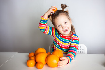 Little girl, 3 year old baby, with a ponytail hairstyle in a colorful colorful striped jacket hugs a lot of appelsins