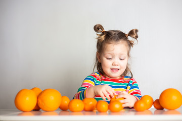 Little girl, 3 year old baby, with a ponytail hairstyle in a colorful colorful striped jacket with a huge number of appelsins and tangerines