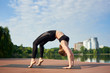 © anatoliy_gleb - Slim girl in black sportswear standing in pose of bridge, asana urdhva dhanurasana in a city park with green trees, lake and buildings in background under blue sky with copy space. Morning training