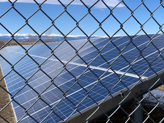 Closeup view of a long solar panel through a chain link fence with mountains in the background.