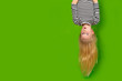Surprised shocked little blonde girl hanging happy upside down over isolated green studio background. Emotion, expression. Copy space for text.
