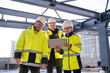 Group of engineers standing outdoors on construction site, using tablet.
