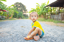 LIttle Asian Boy Sitting On Bluestone Gravel Rock Road In The Evening With Beautiful Sun Warm Light, Naughty Kid Playing On Gravel Stone Pebble Road