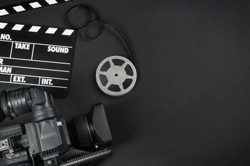 Wall Mural - modern video camera, movie clapper and reel on black background, flat lay. space for text