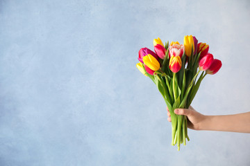 Sticker - Woman holding beautiful spring tulips on light blue background, closeup. Space for text