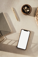 Wall Mural - Blank screen smart phone, stationery on beige background. Flat lay, top view. Styled home office desk workspace. Business, work template.