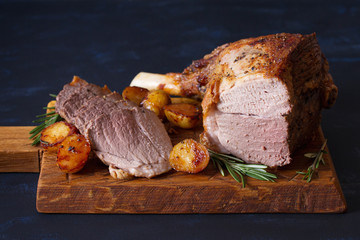 Wall Mural - Roast leg of lamb with potatoes and rosemary on serving wooden board