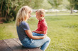 © anoushkatoronto - Young Caucasian mother and boy toddler son sitting together face to face. Family mom and child talking communicating outdoor on a summer day. Happy authentic family childhood lifestyle.
