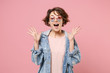 Excited young brunette woman girl in casual denim jacket, eyeglasses posing isolated on pastel pink wall background. People lifestyle concept. Mock up copy space. Keeping mouth open, spreading hands.