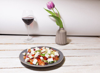 Canvas Print - still life with plate of greek salad,  red wine glass, vase with tulip on white wooden table