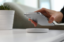 Woman Putting Smartphone On Wireless Charger In Room, Closeup