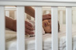 Lovely newborn baby girl sleeping in bed, view through crib bars