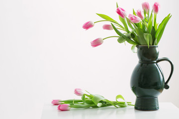 pink tulips on green jug on white background