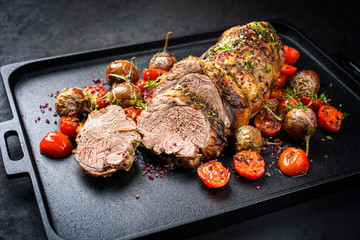 Wall Mural - Traditional barbecue rolled lamb roast sliced with tomatoes and mini eggplant as closeup on a modern design black tray