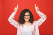 © denis_vermenko - Close-up portrait of surprised pretty young woman in casual pointing with two fingers up, isolated on red background.