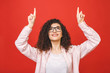 © denis_vermenko - Close-up portrait of surprised pretty young woman in casual pointing with two fingers up, isolated on red background.