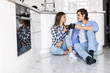 © F8  \ Suport Ukraine - Happy young man and woman sitting on kitchen floor and drinking coffee. Romantic young couple sitting on kitchen floor in morning.