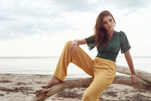 Beautiful Fashionable Girl On The Beach Dressed In A Green Sweatshirt And Yellow Pants, Stylish Retro Clothing, Lifestyle And Fashion