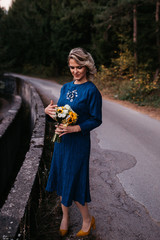 Wall Mural - Portrait of Beautiful elegant bride in blue wedding dress with mid length skirt and long sleeves. Pretty girl in white. Nature, with road, sunset time.