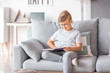 © Pixel-Shot - Little boy wearing glasses while reading book at home