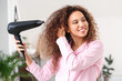 Beautiful young African-American woman with blow dryer at home