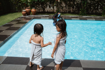 two little girls stand wearing towels after they finish playing in the pool