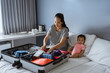 © Odua Images - baby sits beside the mother preparing clothes to put in the suitcase