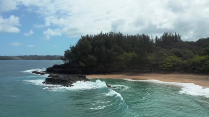 Wall Mural - Aerial drone shot flying toward the rock at one end of the coast over Lumaha'i beach on Hawaiian island of Kauai with Hanalei in the distance