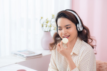 Young Asian woman listening to music and eating macarons.