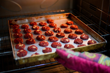 Baker taking out a tray of red velvet cookies from the oven.