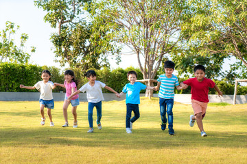 Wall Mural - Large group of happy Asian smiling kindergarten kids friends holding hands playing and running in the park on sunny summer day in casual clothes..