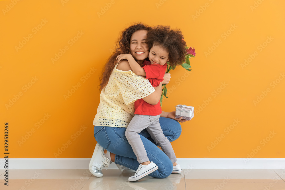 Little African-American girl greeting her mother near color wall - obrazy, fototapety, plakaty 