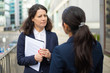 © Mangostar - Serious businesswomen talking on street. Professional female colleagues in formal wear standing on urban city street and discussing work. Cooperation concept
