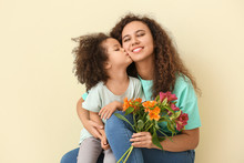 Little African-American Girl With Her Mother And Bouquet On Color Background