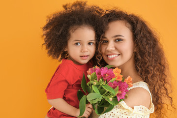 Wall Mural - Little African-American girl with her mother and bouquet on color background