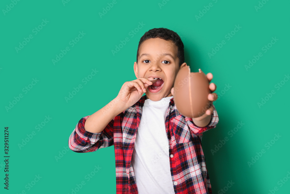 Cute African-American boy with sweet chocolate egg on color background