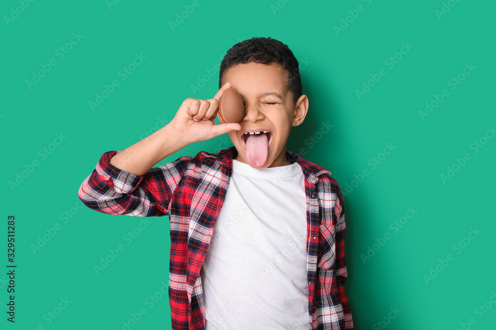 Cute African-American boy with sweet chocolate egg on color background