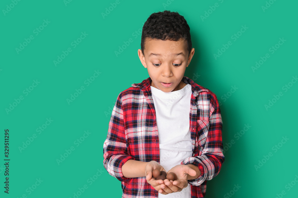 Surprised African-American boy with sweet chocolate eggs on color background