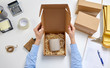 delivery, mail service, people and shipment concept - female hands packing mug to parcel box with straw filler at post office